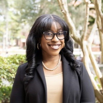 A woman is wearing glasses while smiling outdoors. 